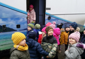 Widok na grupę dzieci wsiadających do autokaru.
